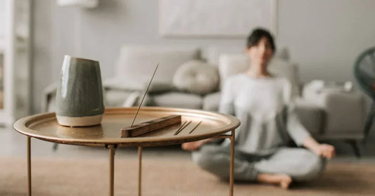 Incenso a arder numa mesa, com pessoa a meditar ao fundo