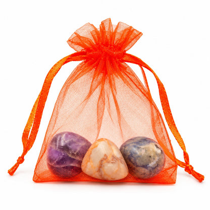 Bolsa laranja translúcida com cordão e três pedras roladas, sobre fundo branco.