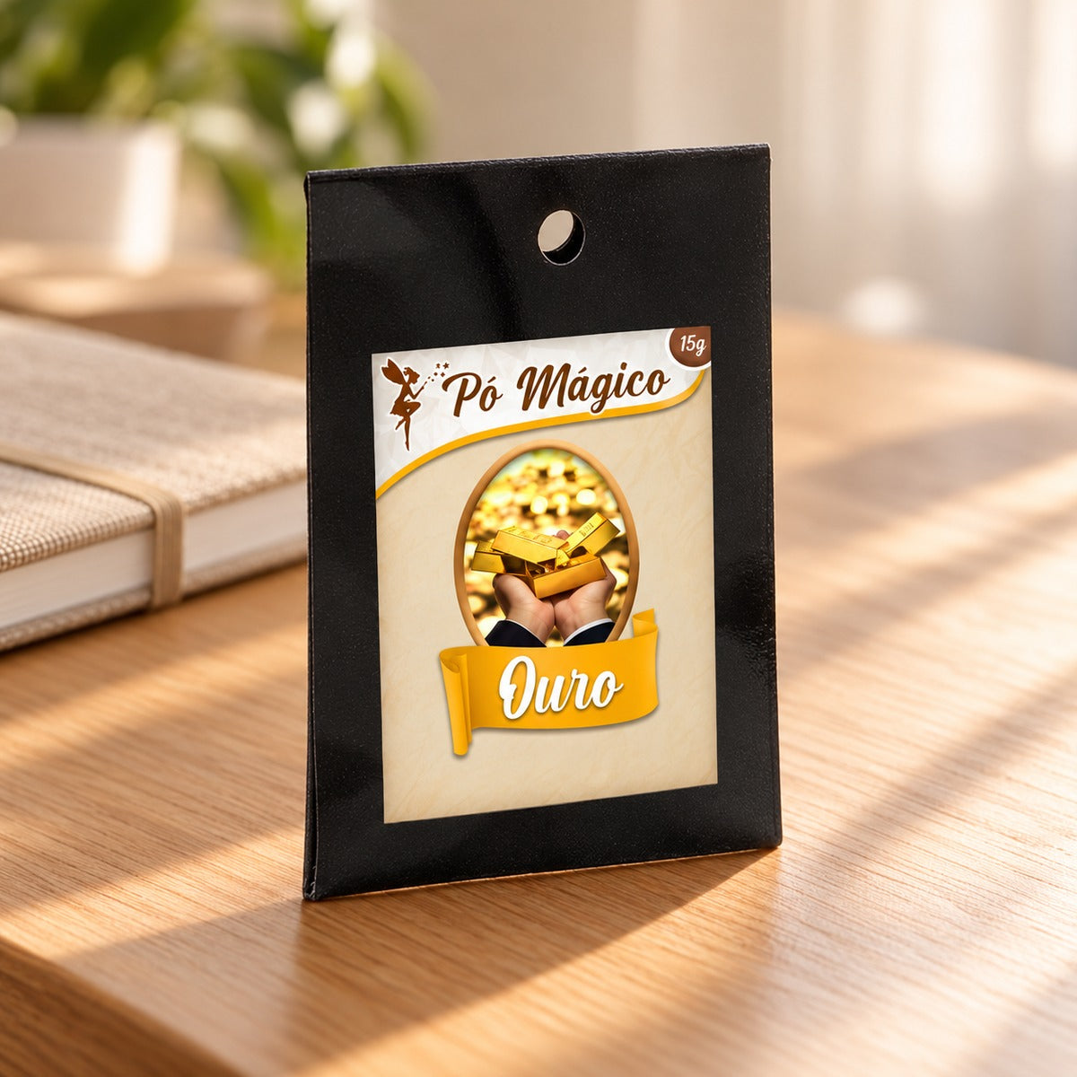 Embalagem de Pó Mágico Ouro de 15 g sobre uma mesa de madeira, junto a um caderno.